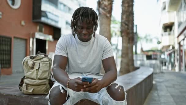 Afrykański Amerykanin Pomocą Smartfona Siedzi Ławce Ulicy — Wideo stockowe