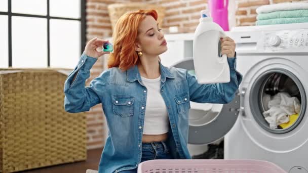 洗濯室で洗剤ボトルを選択する服を洗濯する若い赤毛の女性 — ストック動画