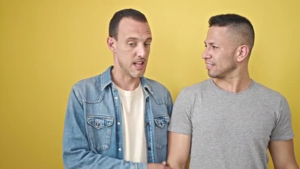 隔離された黄色の背景の上に側を指す驚きの表情で立っている2人の男性カップル — ストック動画
