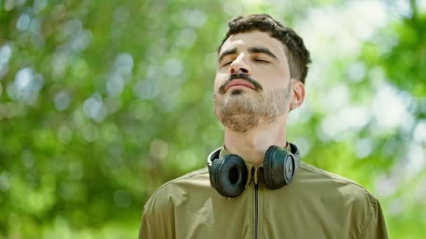 Νεαρός Ισπανός Χαμογελάει Αυτοπεποίθηση Φορώντας Ακουστικά Που Αναπνέουν Στο Πάρκο — Αρχείο Βίντεο