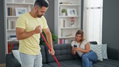Erkek ve kadın ev işi yaparken, kız arkadaş evde akıllı telefon kullanıyor.