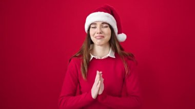Genç İspanyol kadın, Noel şapkası takıp şans diliyor. Kırmızı arka plan için dua ediyor.
