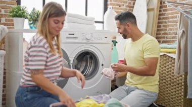 Man and woman couple smiling confident washing clothes at laundry room