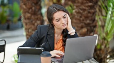 Genç ve güzel İspanyol iş kadını. Laptop ve dokunmatik ped kullanıyor. Kahve dükkanının terasında yorgun.