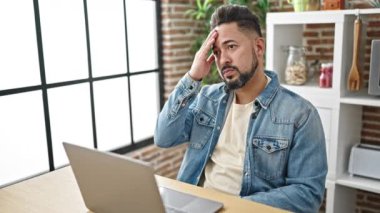 Genç latin adam yemek odasındaki masada dizüstü bilgisayar kullanarak strese girdi.