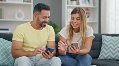Kadın ve erkek, evdeki koltukta oturan akıllı telefonları kullanıyor.