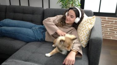 Köpekli genç İspanyol kadın evdeki kanepede uzanıp müzik dinliyor.
