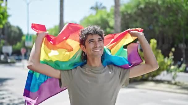 若いヒスパニックの男は自信を持って街頭で虹の旗を保持しています — ストック動画