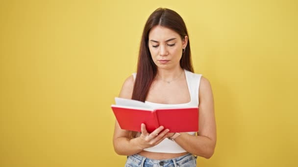 若い美しいヒスパニック系女性は 孤立した黄色の背景について考える本を読む — ストック動画