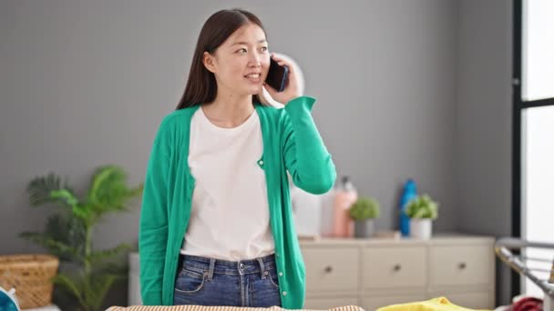 Genç Çinli Kadın Akıllı Telefonda Konuşuyor Çamaşırhanede Giysileri Ütülüyor — Stok video