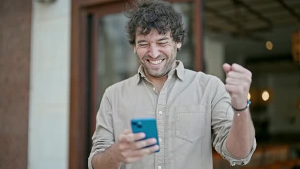 Junger Hispanischer Mann Lächelt Selbstbewusst Mit Smartphone Und Siegergeste Auf — Stockvideo