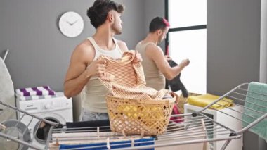 Çamaşır yıkayan iki adam çamaşır odasına kıyafet atıyor.