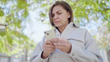 Orta yaşlı İspanyol kadın parkta akıllı telefon kullanıyor.
