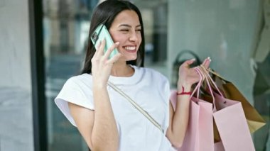 Genç, güzel İspanyol bir kadın elbise mağazasında akıllı telefondan konuşuyor.