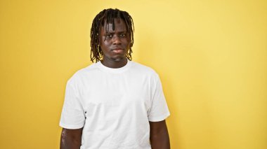 İzole edilmiş sarı arka plan üzerinde ciddi bir ifadeyle duran Afrikalı Amerikalı adam.