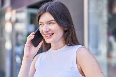 Beyaz bir kadın gülümsüyor ve caddede akıllı telefondan konuşuyor.