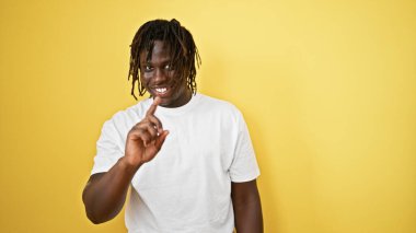 Afro-Amerikalı adam, izole edilmiş sarı arka planda gülümseyen parmaklarıyla hayır diyor.
