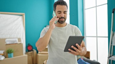 Genç İspanyol adam akıllı telefondan konuşuyor. Yeni evinde dokunmatik ped kullanıyor.