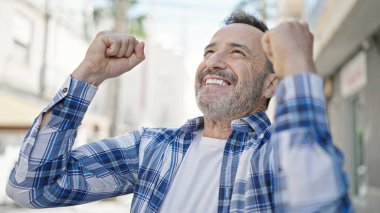 Orta yaşlı adam gökyüzüne bakıyor. Sokakta kazanan yüz ifadesiyle.