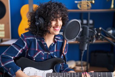 Ortadoğulu genç bir kadın sanatçı müzik stüdyosunda gitar çalarak şarkı söylüyor.