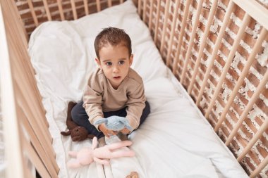 Sevimli İspanyol çocuk yatak odasında beşikteki bebeği tutuyor.