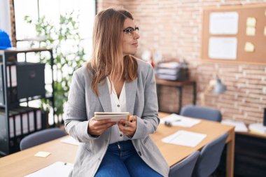Young hispanic woman working at the office wearing glasses looking to side, relax profile pose with natural face and confident smile. 
