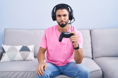 Kanepede oturmuş video oyunu oynayan İspanyol genç adam depresif ve endişeli, sinirli ve korkmuş bir şekilde oturuyor. hüzünlü ifade. 
