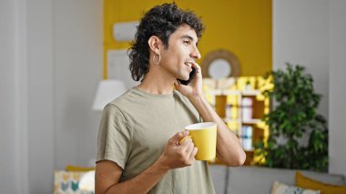 Genç İspanyol adam akıllı telefonda konuşuyor. Evde kahve içiyor.