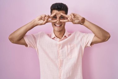 Pembe arka planda duran genç İspanyol adam barış sembolü yapıyor. Yüzünde parmakları, gülümseyerek zaferi gösteriyor. 