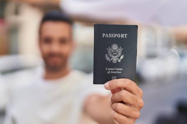 Young hispanic man smiling confident holding passport at street