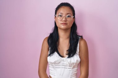 Yüzünde ciddi bir ifadeyle pembe arka planda duran Asyalı genç bir kadın. Basit ve doğal bir şekilde kameraya bakıyorsun.. 