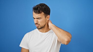 İzole edilmiş mavi arka planda servikal ağrısı olan genç İspanyol bir adam.