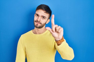 Mavi arka planda dikilen İspanyol adam parmağını kaldırmış ve kızgın bir ifadeyle işaret ediyor, hiçbir hareket göstermiyor. 