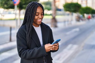 Afro-Amerikalı kadın sokakta akıllı telefon kullanarak kendine güveniyor.