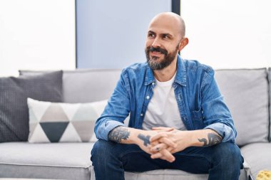 Young bald man smiling confident sitting on sofa at home
