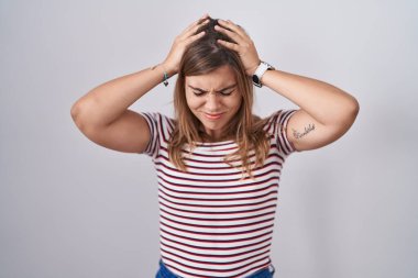 Genç İspanyol kadın izole edilmiş arka planda duruyor. Baş ağrısı, acı ve migren yüzünden çaresiz ve stresli. Eller başının üstünde.. 