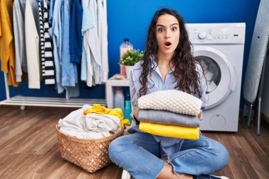 Genç esmer kadın temiz çamaşırları tutuyor. Şaşırmış ve şaşırmış bir ifade, korku ve heyecanlı bir yüz ifadesi var.. 