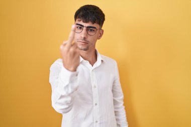 Young hispanic man standing over yellow background showing middle finger, impolite and rude fuck off expression 