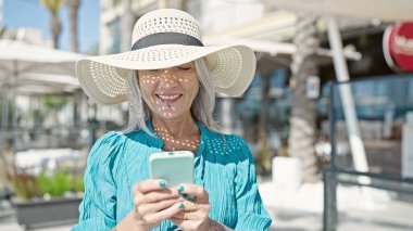 Orta yaşlı gri saçlı turist kahve dükkanının terasında akıllı telefon kullanarak gülümsüyor.