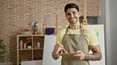 Genç İspanyol ressam gülümsüyor. Sanat stüdyosunda renkleri karıştırıyor.