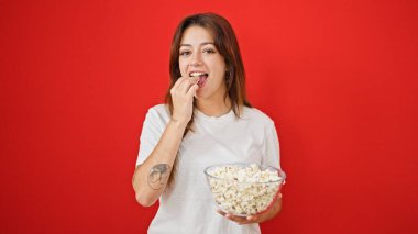Genç, güzel İspanyol bir kadın patlamış mısır yiyor. Kırmızı arka planda gülümsüyor.
