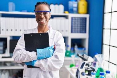 Afrikalı Amerikalı bilim kadını gülümsüyor. Laboratuvarda elinde bir pano var.