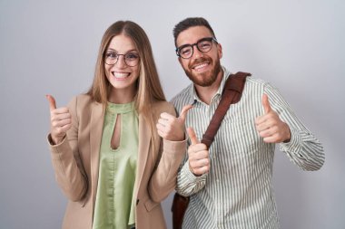 Beyaz arka plan başarı işaretinin üzerinde duran genç çift elleriyle olumlu jest yapıyor, gülümsüyor ve mutlu. Neşeli ifade ve kazanan jest. 