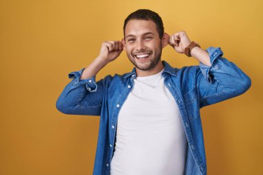 Sarı arka planda dikilen İspanyol adam gülümsüyor parmaklarıyla kulaklarını çekiyor, komik bir jest. deneme sorunu 