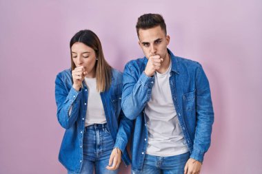 Young hispanic couple standing over pink background feeling unwell and coughing as symptom for cold or bronchitis. health care concept. 