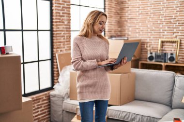 Young woman smiling confident using laptop at new home