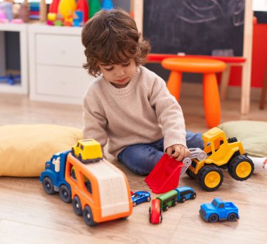 Anaokulunda yerde oturan sevimli İspanyol çocuk araba oyuncağıyla oynuyor.