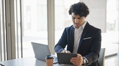 Young latin man business worker using laptop and touchpad at office