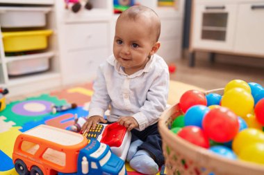 Anaokulunda yerde taşaklarıyla oynayan sevimli beyaz çocuk.