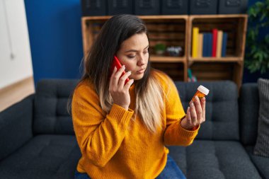Young beautiful plus size woman talking on smartphone holding pills at home